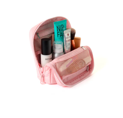 Close-up flat lay of a pink makeup bag unzipped to show internal storage filled with various cosmetics and brushes.