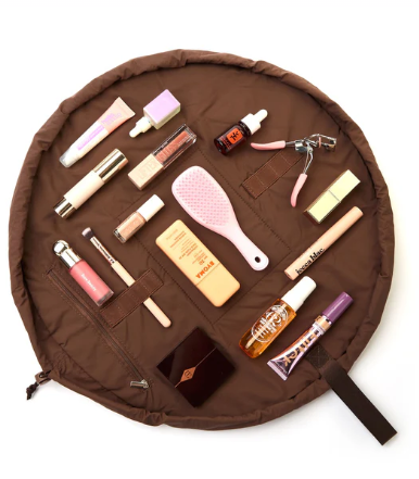 Overhead flat lay of a brown circular drawstring makeup mat fully spread out, displaying neatly arranged beauty tools like a hairbrush and foundation.