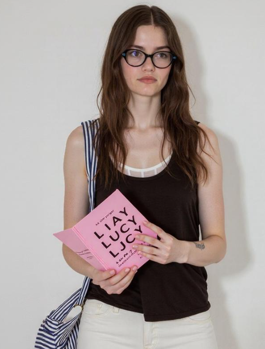 Original reference photo of a woman with glasses holding a pink book titled "LIAY LUCY" for AI stylization.