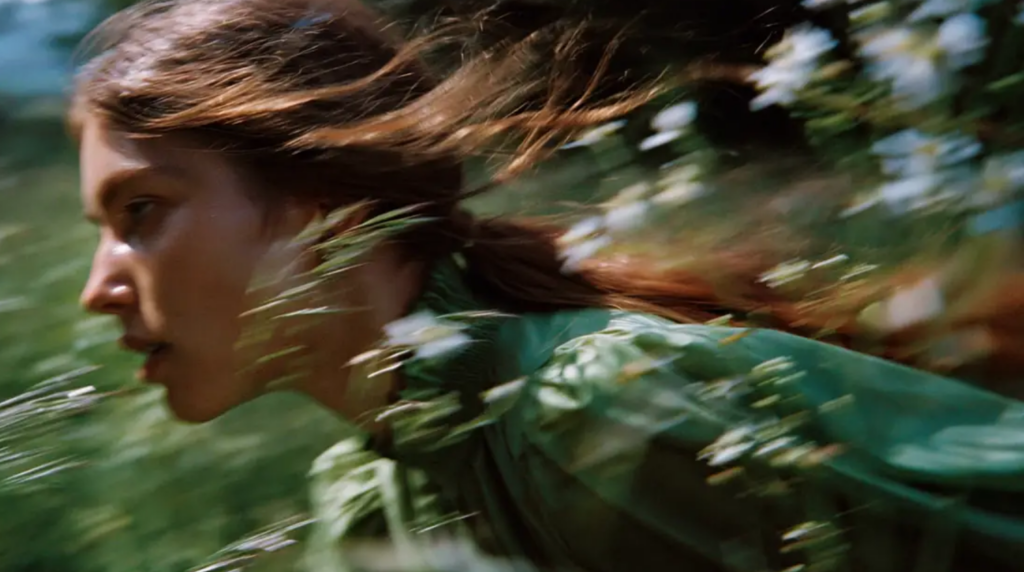 A motion-blur cinematic shot of a woman in a green dress running through a meadow, created with Midjourney v7.