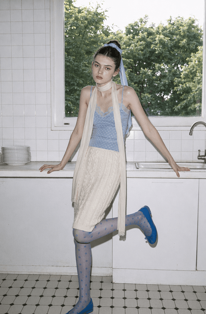 Clean aesthetic Korean fashion lookbook photo of an AI model in a blue lace top and knit skirt standing in a minimalist white-tiled kitchen.
