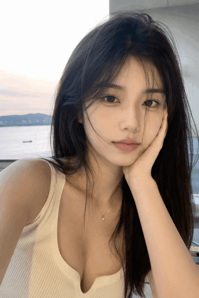 High-quality selfie of a young Asian woman leaning on her hand with an ocean sunset background.