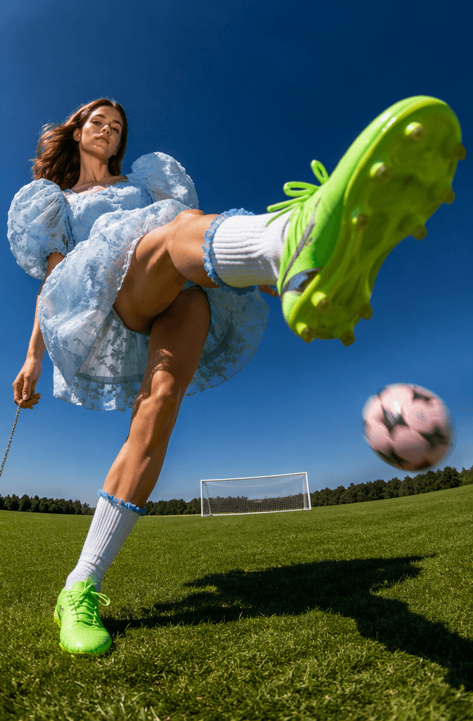 cup7 – WeShop AI Blog Dynamic football fashion image showing a model in a blue dress and bright green cleats kicking toward the camera on a football field.