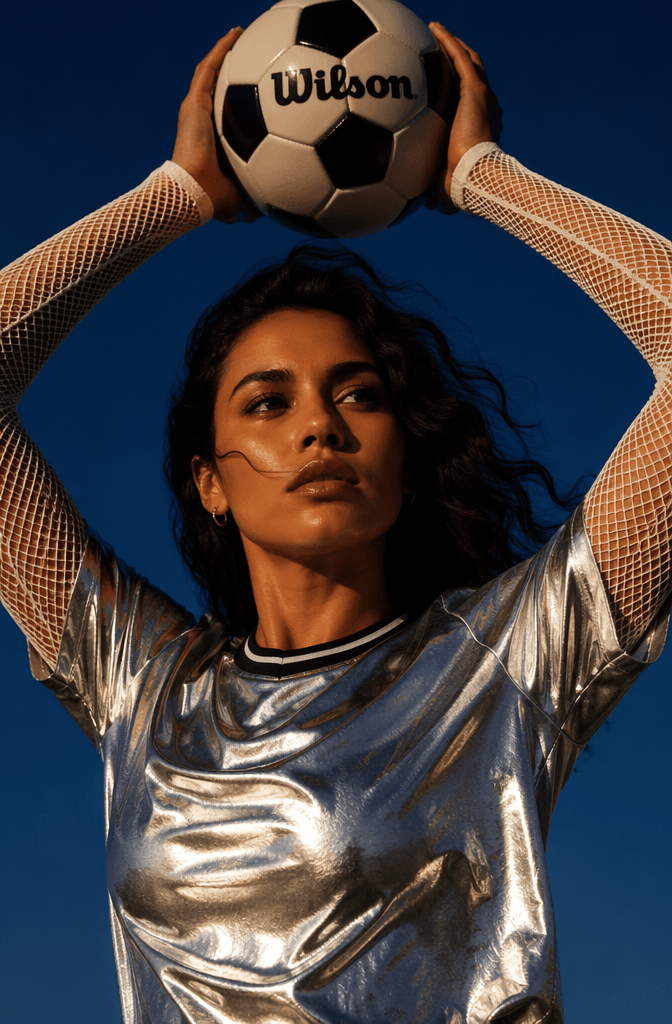 cup8 – WeShop AI Blog High fashion football editorial image showing a model in a metallic silver top holding a football above her head against a deep blue background.