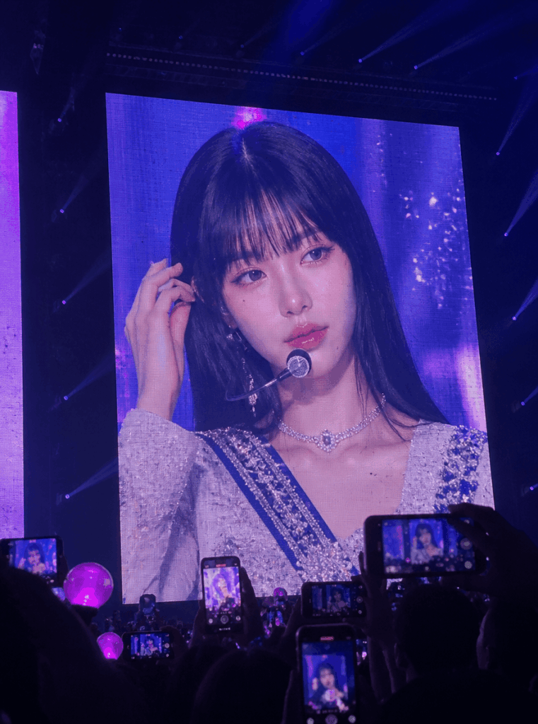 K-pop concert screen fan-cam image with audience phones, purple lights, and a giant LED display