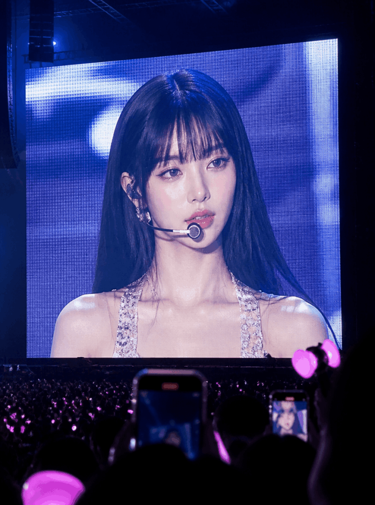 K-pop concert screen example with a black-haired idol on a giant LED screen and lightsticks in the crowd
