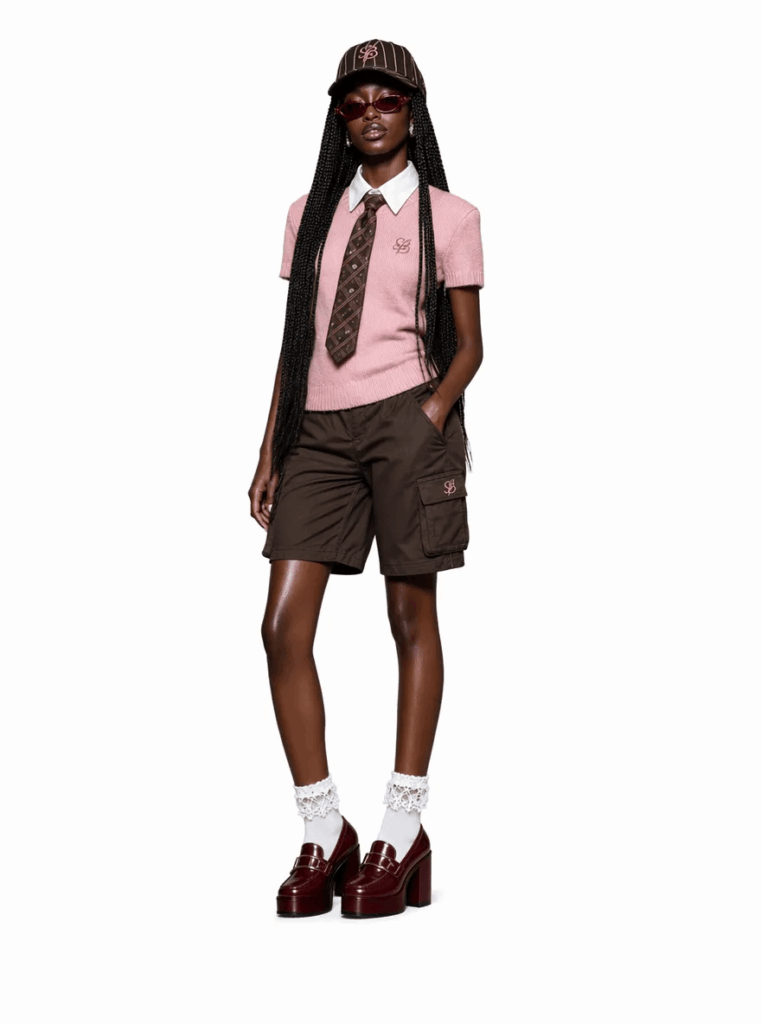 玩偶2 – WeShop AI Blog Full-body fashion portrait of a woman wearing a pink knit top, brown shorts, cap, red sunglasses, and burgundy loafers.