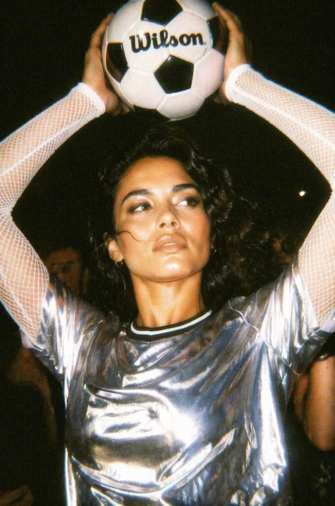Retro 2000s digital camera version of a woman holding a soccer ball with flash lighting, grain, and warm nostalgic tones.