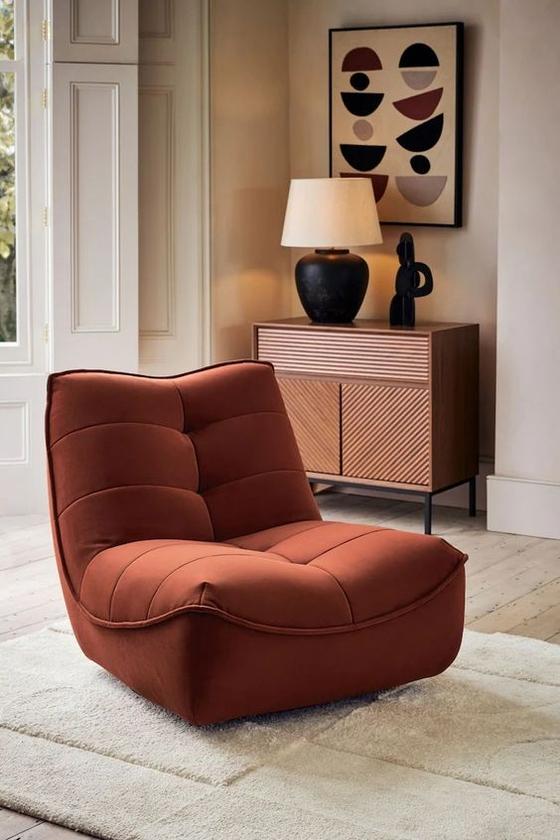 Rust-colored lounge chair photographed in a warm home interior before background removal.