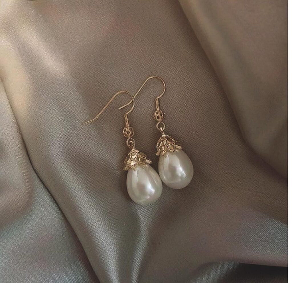 67f4a6cc394c3689928c9014_final – WeShop AI Blog Pearl drop earrings on satin fabric after AI Relight with brighter, warmer illumination.