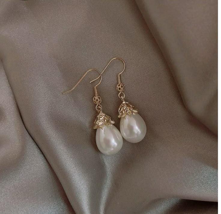 67f4a6cc394c3689928c9014_original – WeShop AI Blog Pearl drop earrings on satin fabric before AI Relight with softer, darker lighting.
