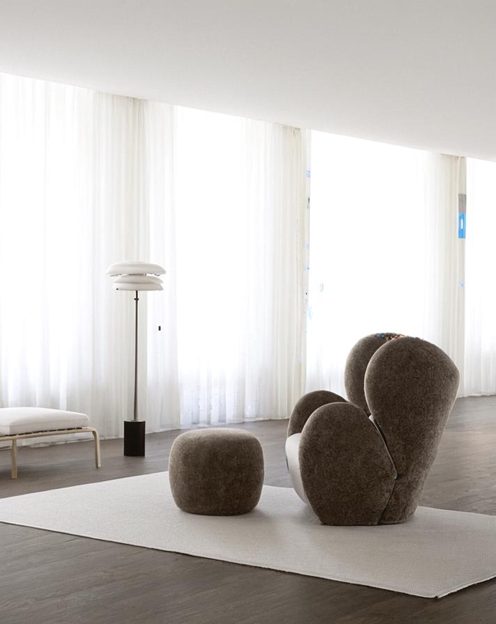 Bright minimalist living room with sculptural brown seating, a floor lamp, white curtains, and a neutral rug.