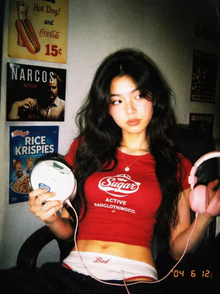 Woman in a red crop top holding headphones in a softly lit bedroom.
