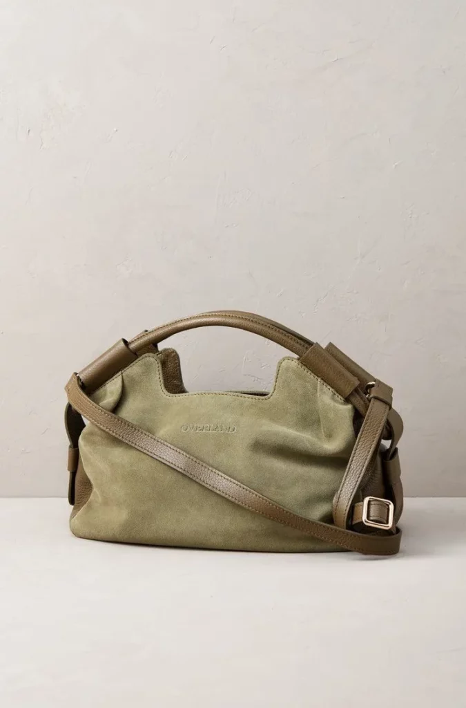 Soft sage green leather handbag displayed against a light neutral studio background with visible grain, seams, and metal hardware.