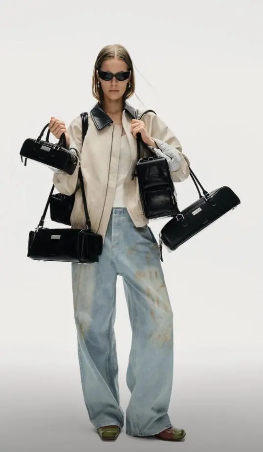 pdcs – WeShop AI Blog Fashion model wearing a modern neutral outfit while carrying several black handbags in a clean studio campaign.