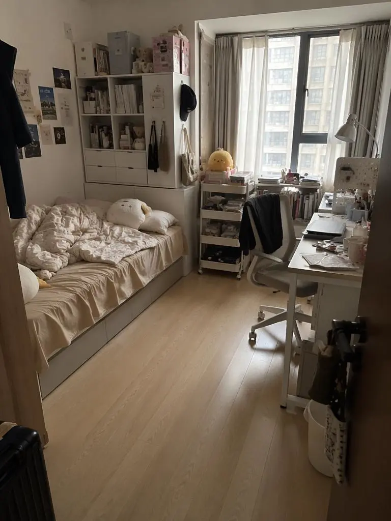 Small bedroom before editing with a bed, desk, shelves, and a crowded workspace near the window