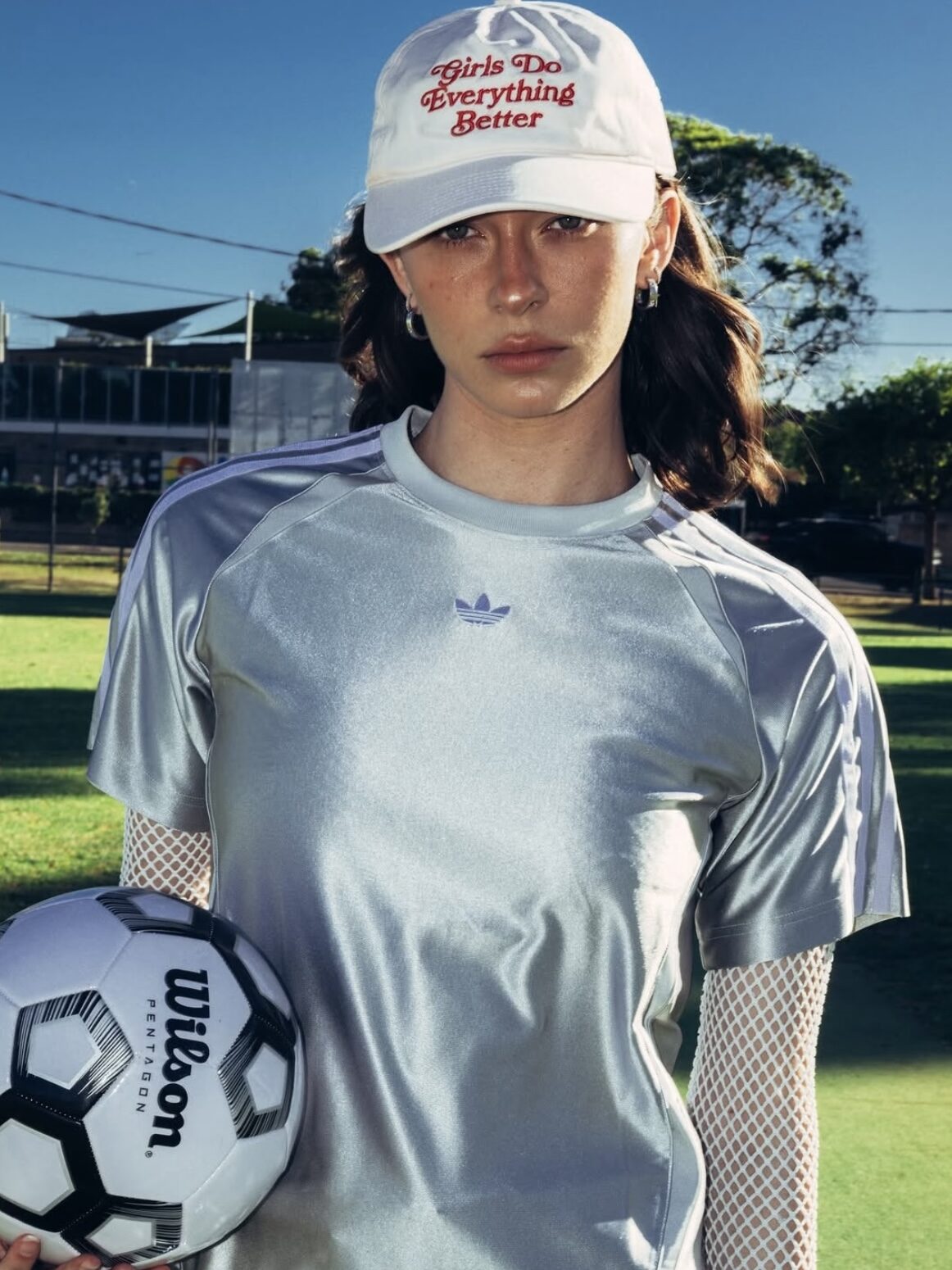 A young woman wearing a white cap holds a soccer ball on a sunny field before using Polaroid Filter Online.