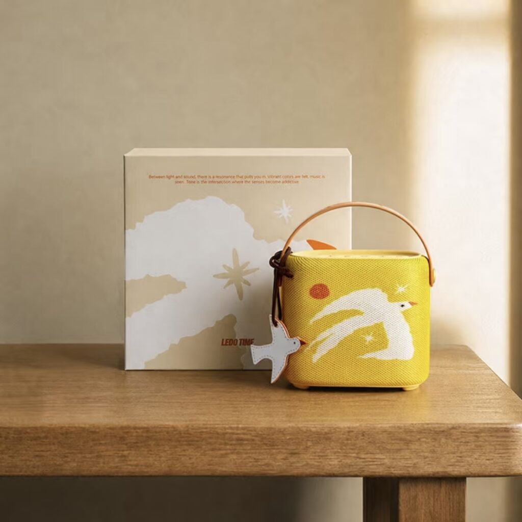Small yellow handled product box displayed on a wooden shelf beside a decorative printed card in warm sunlight.