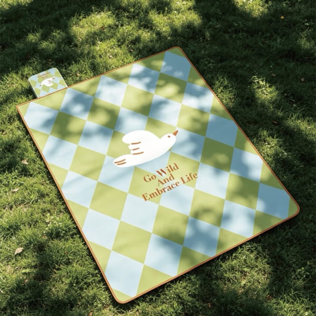 Green and white checkered picnic blanket arranged on sunlit grass with soft tree shadows.